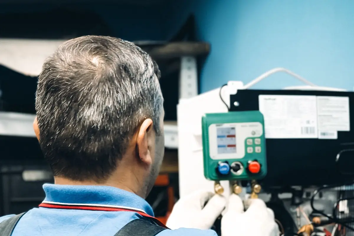 Technician in a blue shirt working on a wall-mounted HVAC control panel