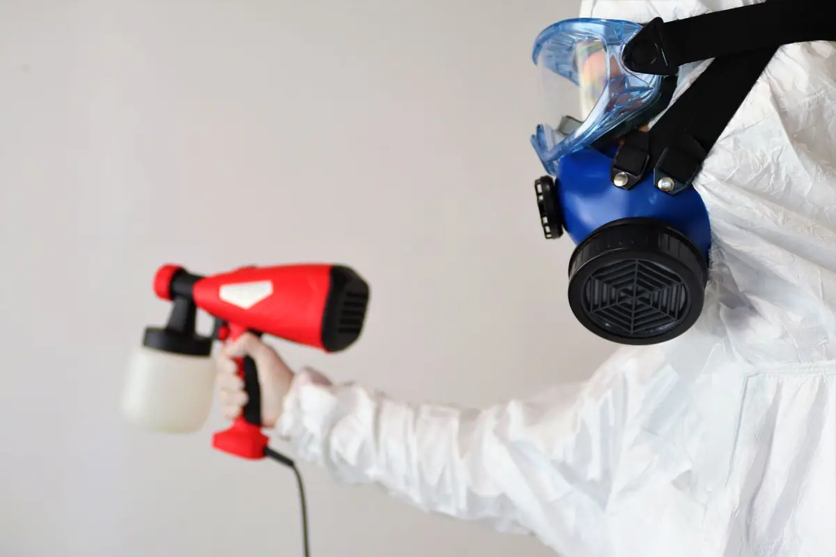 Worker in a white protective suit and full-face respirator using a spray applicator